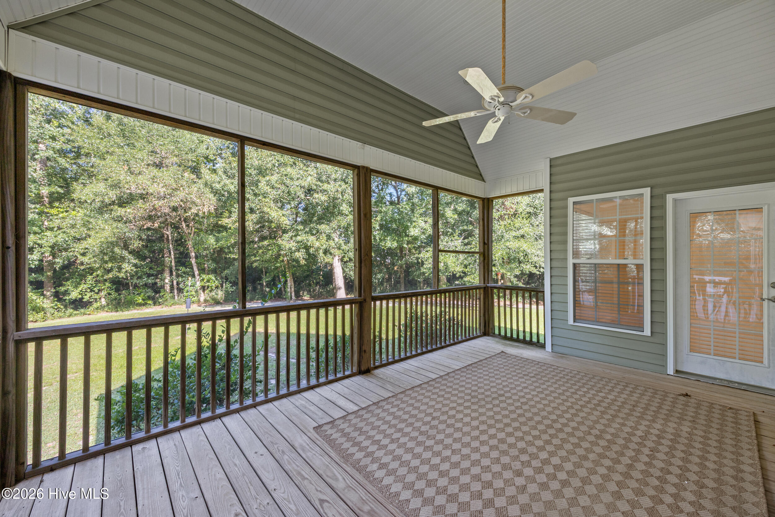 Screened porch with wood decking, a ceiling fan, and a leafy wooded view.