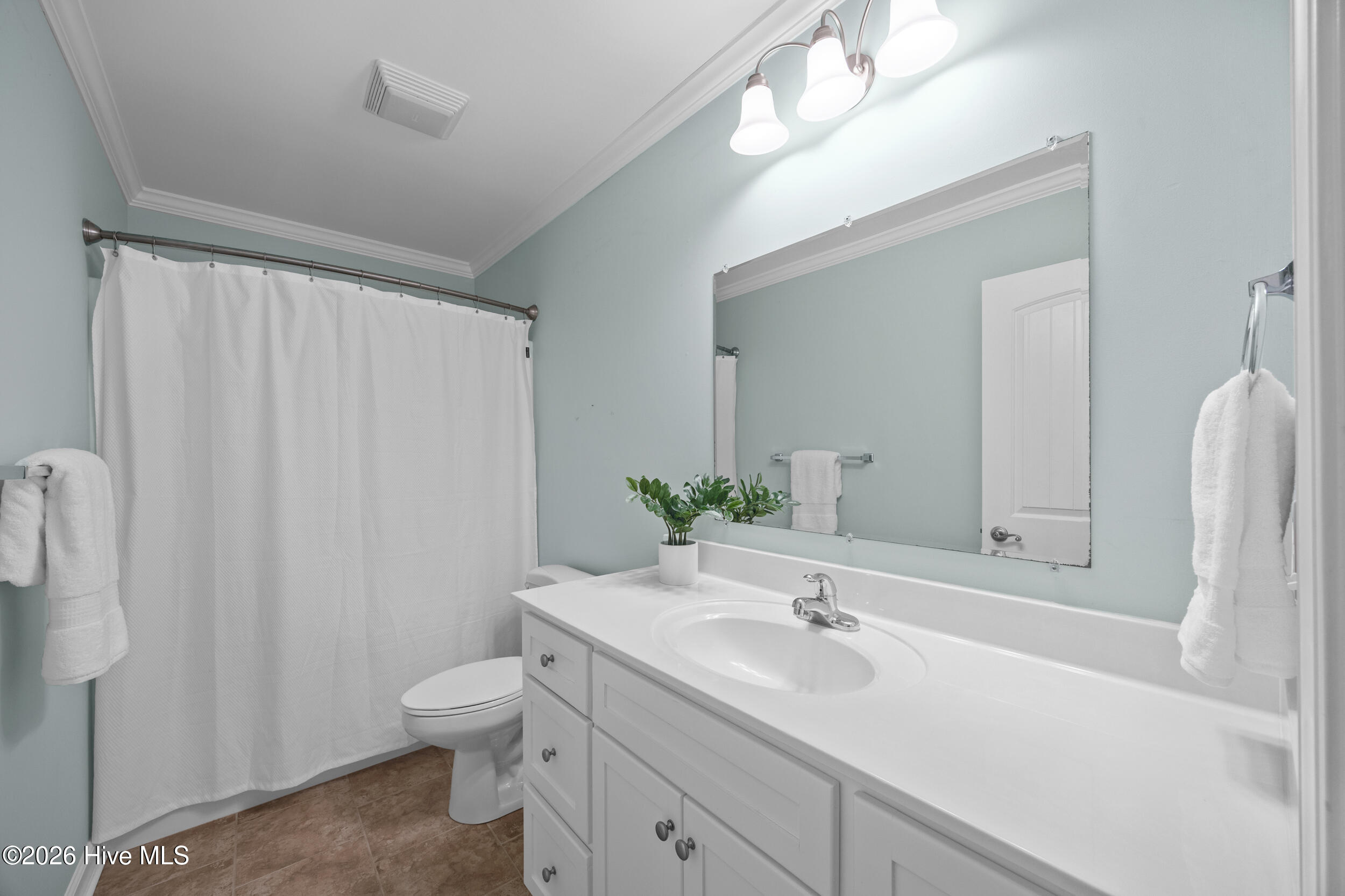Bathroom with a long white vanity, large mirror, curtained shower, and brown tile floor.