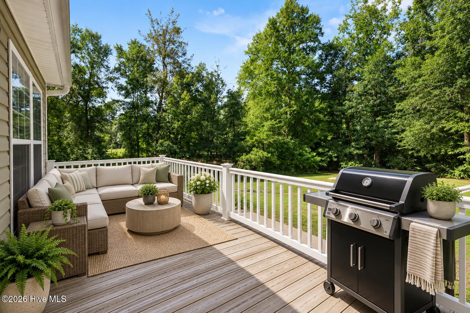 Outdoor deck with wicker seating and a gas grill overlooking a tree-lined lawn.
