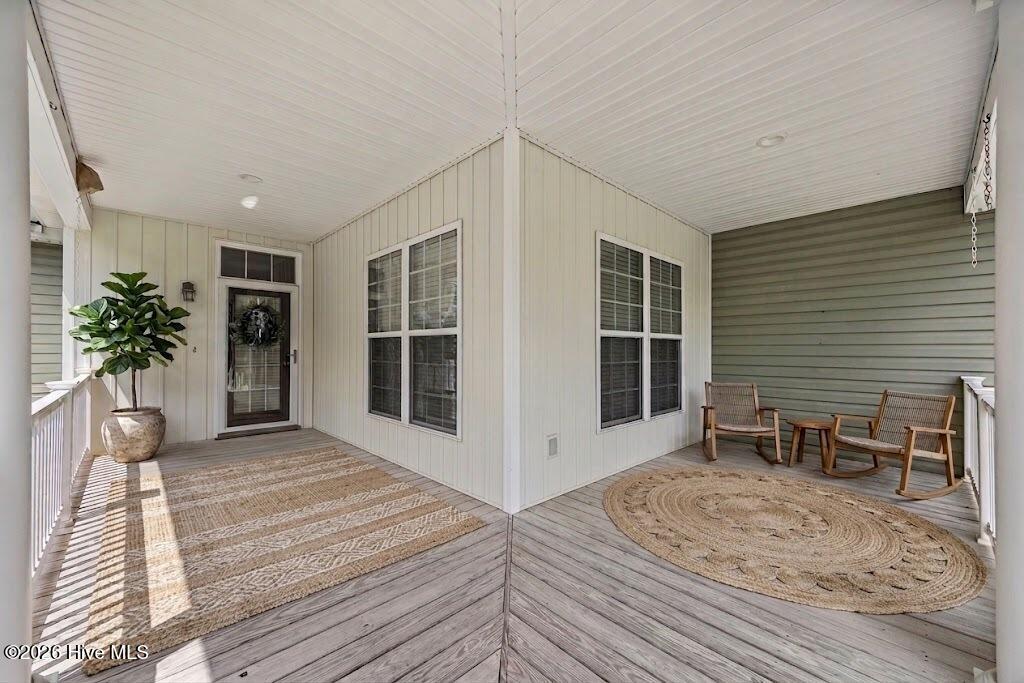 Covered front porch with a glass storm door, potted plant, wicker chairs, and woven rugs.
