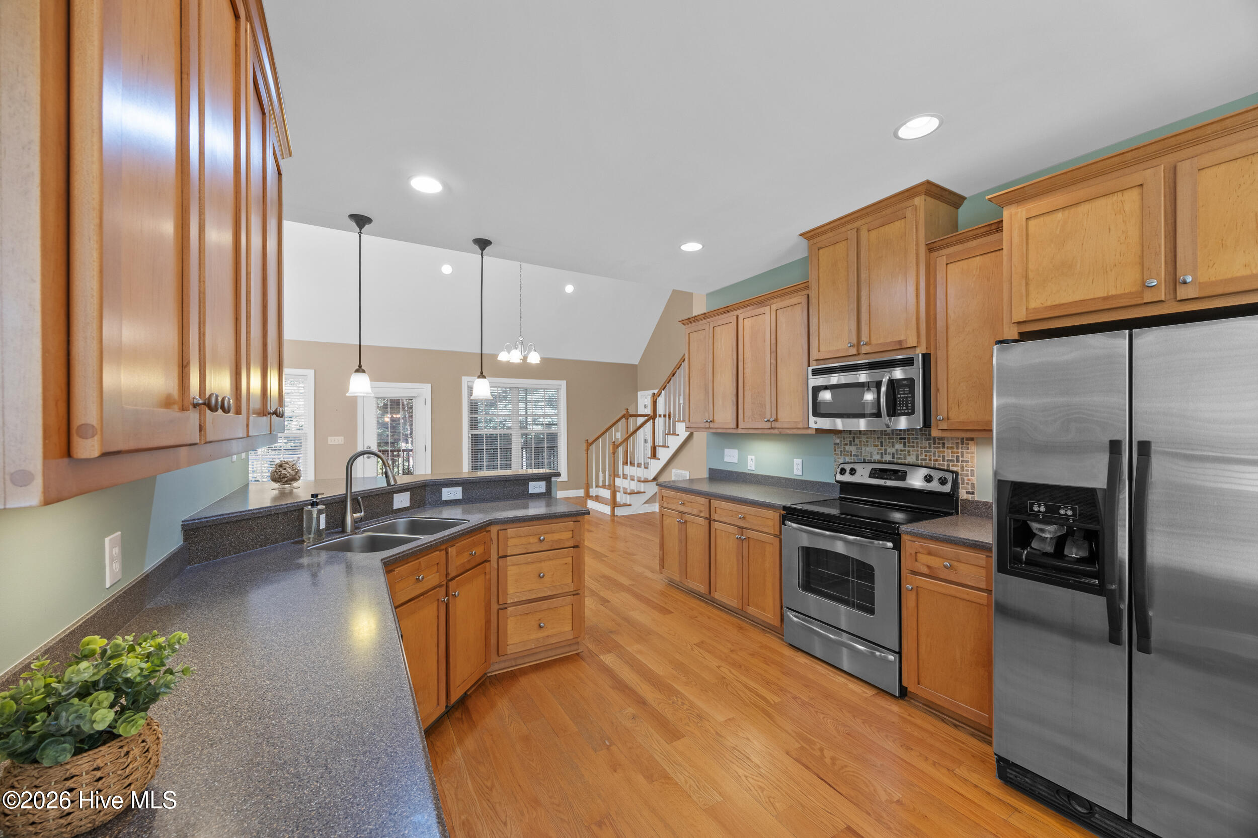 Kitchen with wood cabinets, stainless steel appliances, dark counters, and a sink peninsula overlooking a staircase.