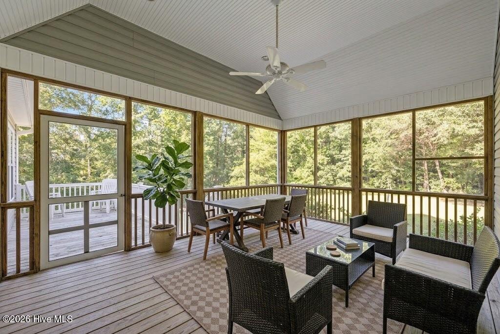 Screened porch with wicker seating, a dining table, and wooded views.