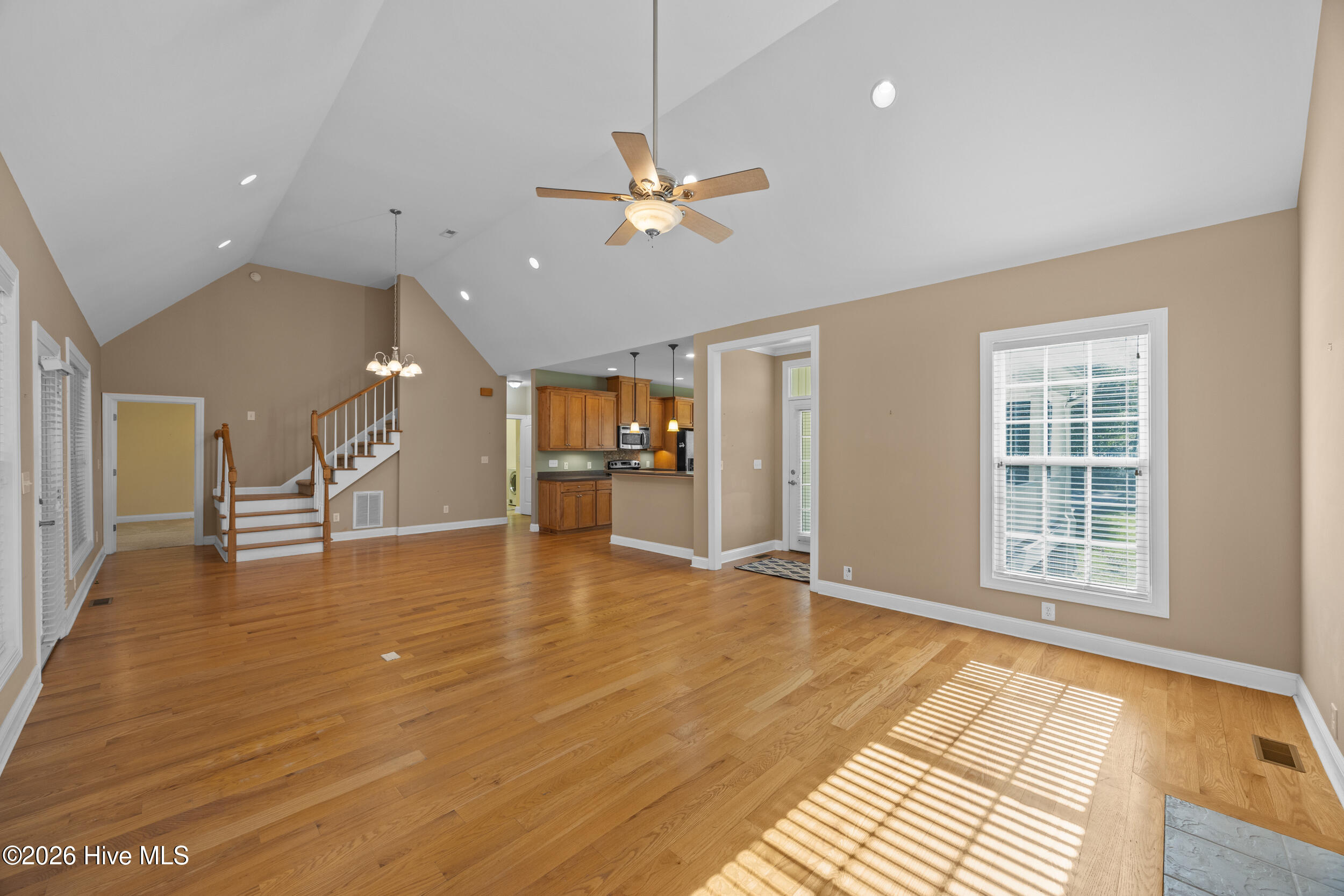 Open living area with hardwood floors, vaulted ceiling, staircase, and sunlight through a window.