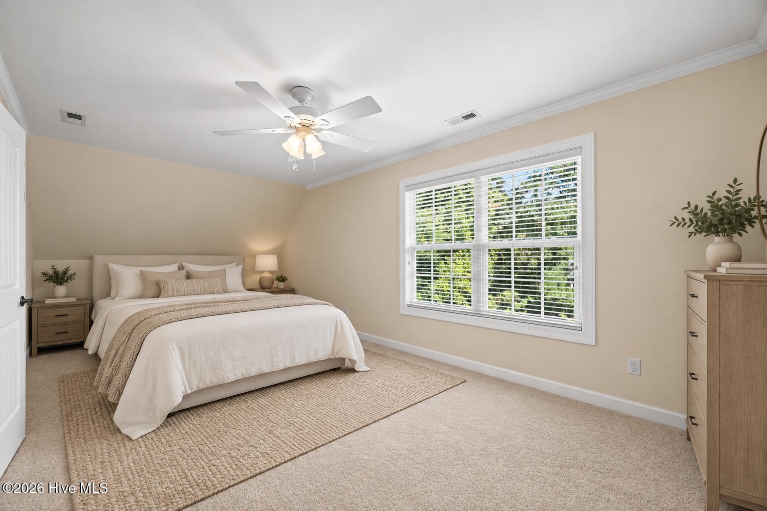 Staged bedroom with a white bed, textured rug, and large window with blinds.