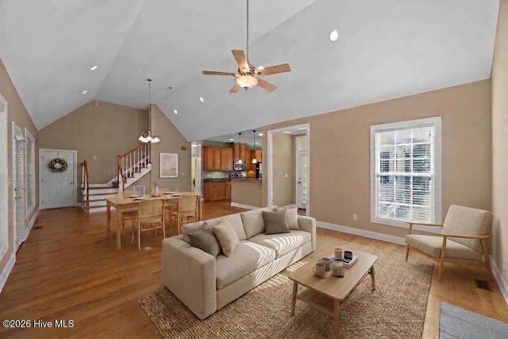 Furnished living room with a vaulted ceiling, hardwood floors, and an open dining area and kitchen.