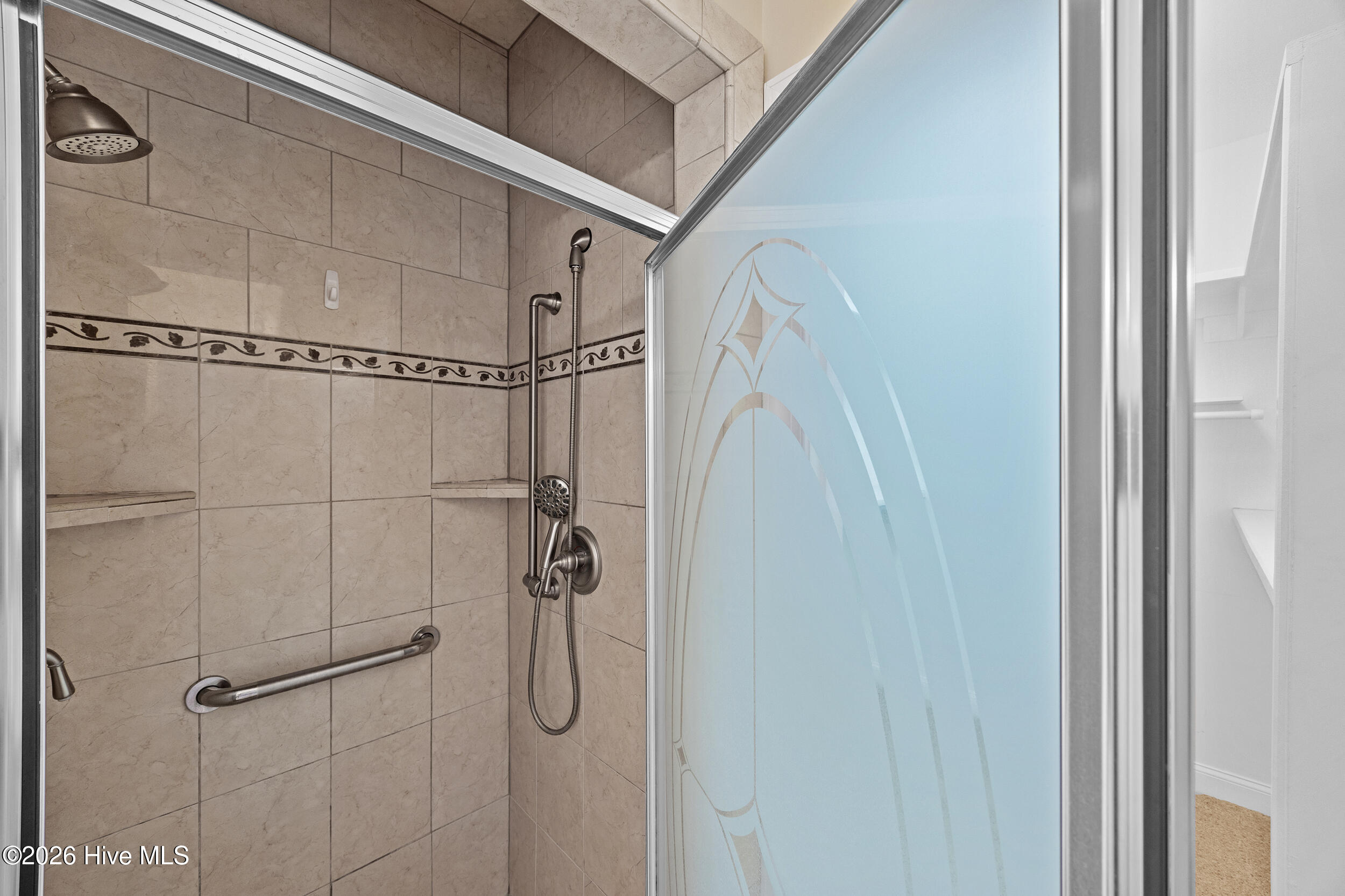 Tiled walk-in shower with frosted glass door, handheld showerhead, and grab bar.