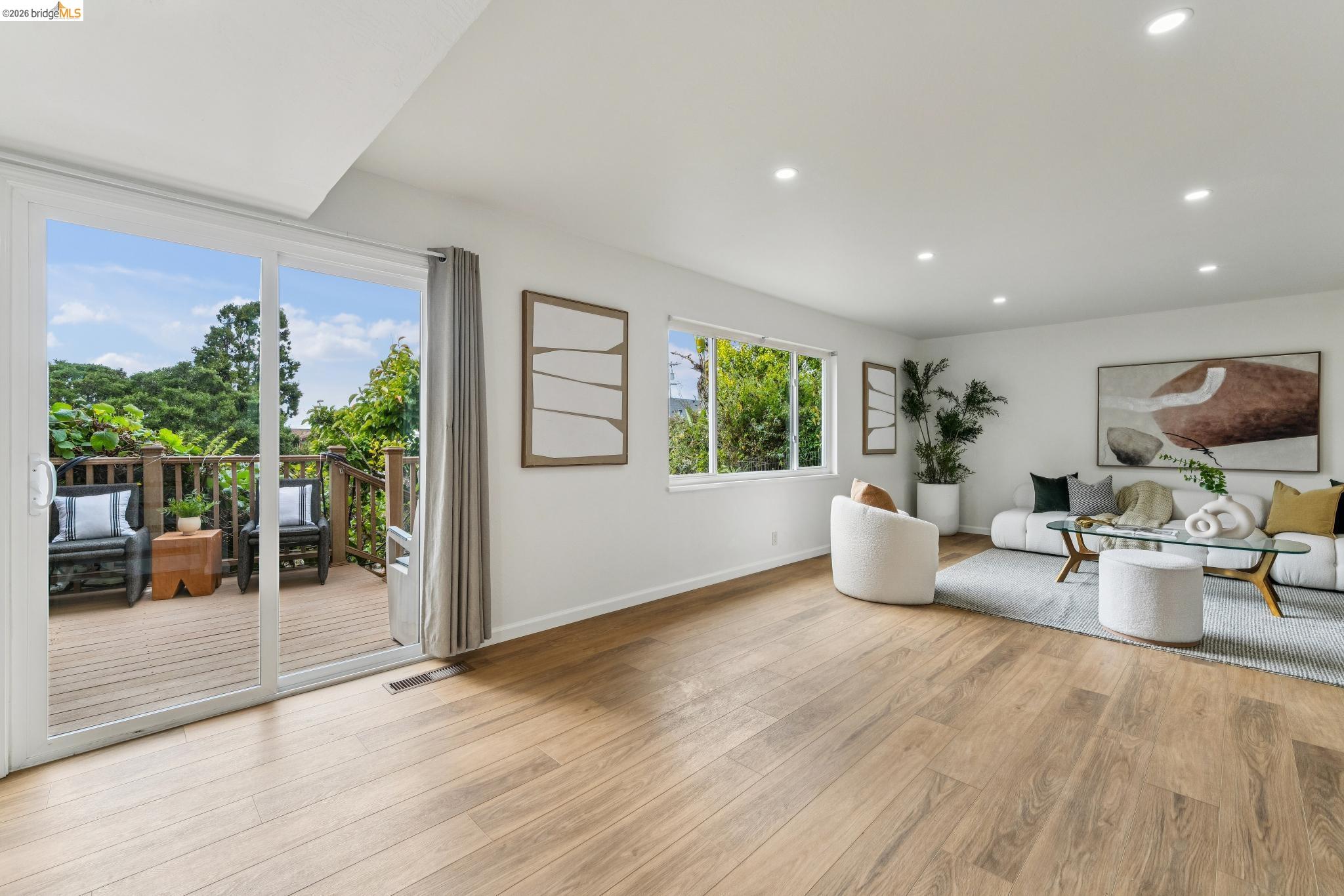 Furnished living room with a white sectional and sliding doors opening onto a leafy deck.