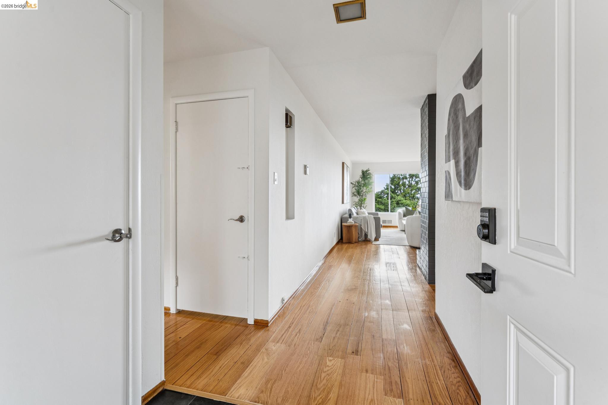 Entry hallway with long hardwood floors leading to a living room and large window.