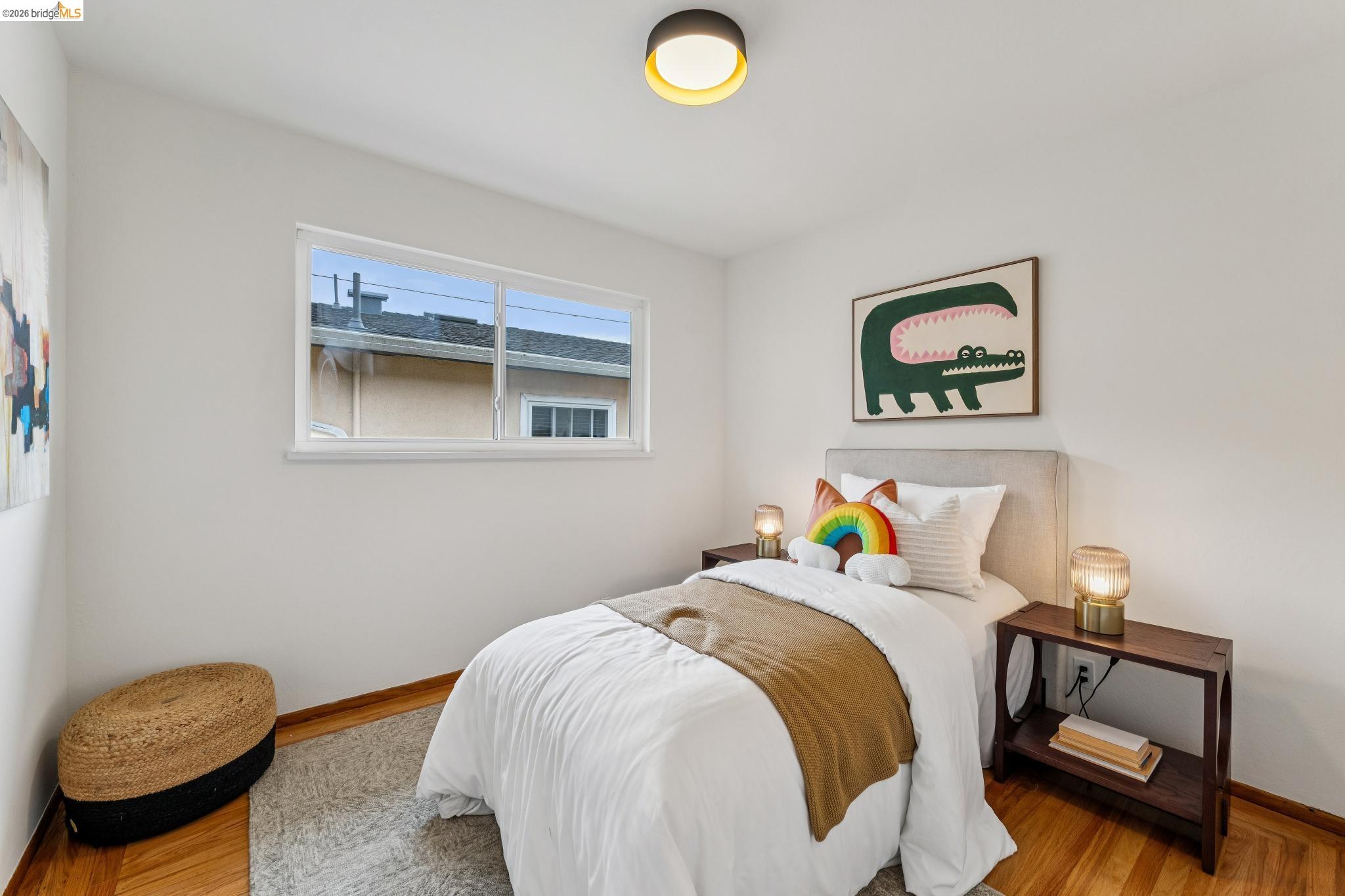 Staged bedroom with a white bed, rainbow pillow, and framed crocodile artwork.