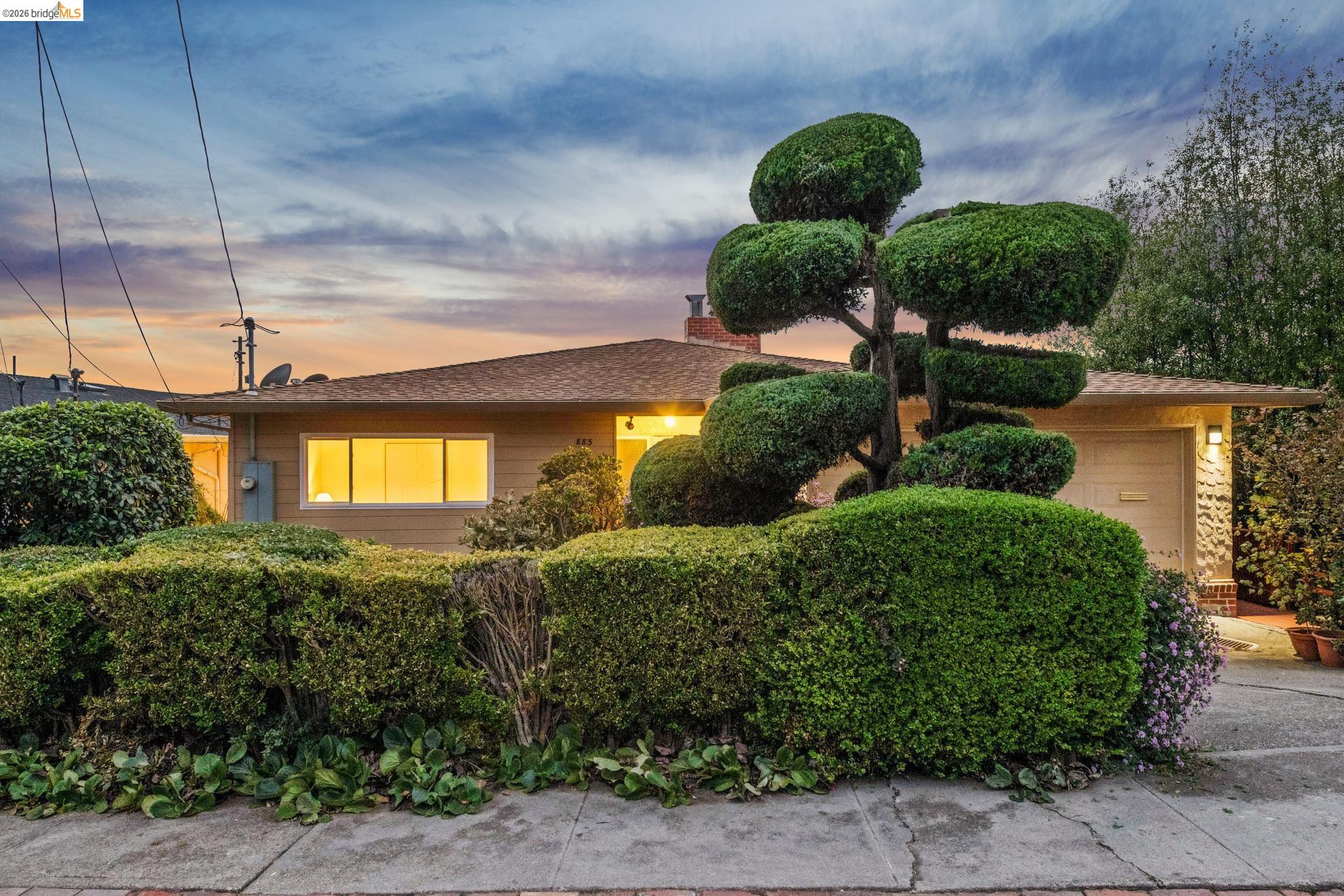 Single-story home at dusk with a garage and sculpted topiary hedges