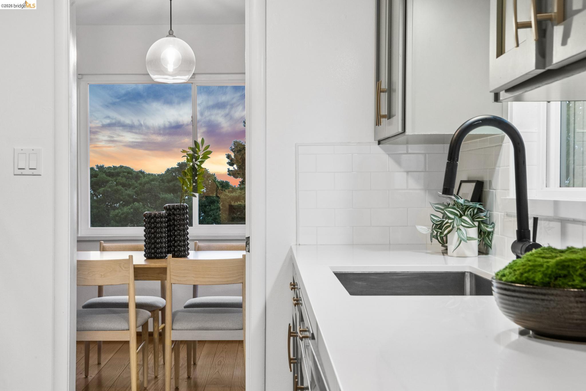 White kitchen with a black gooseneck faucet opening onto a dining area with a sunset view.