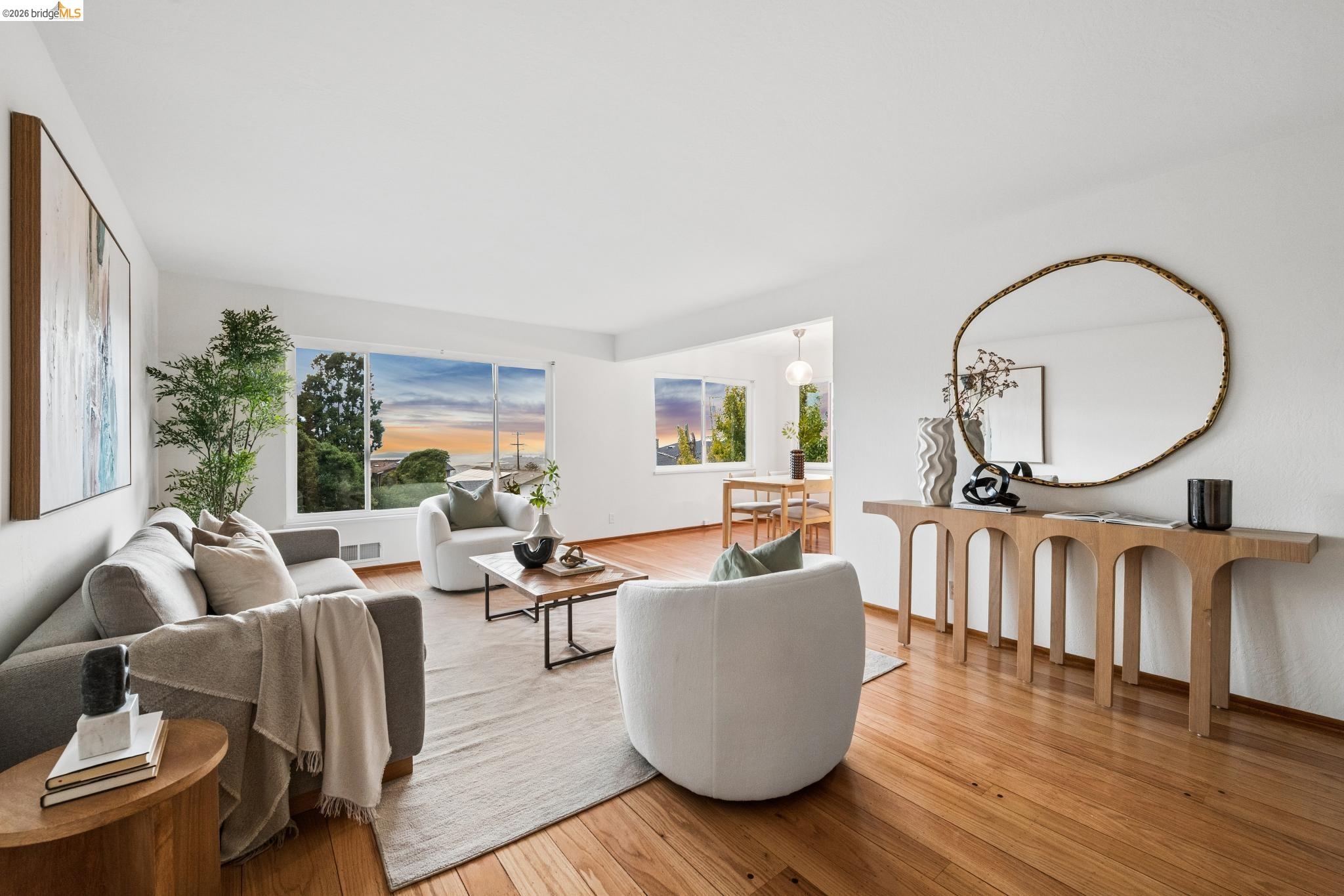 Staged living room with hardwood floors, neutral seating, and sunset light through wide windows.
