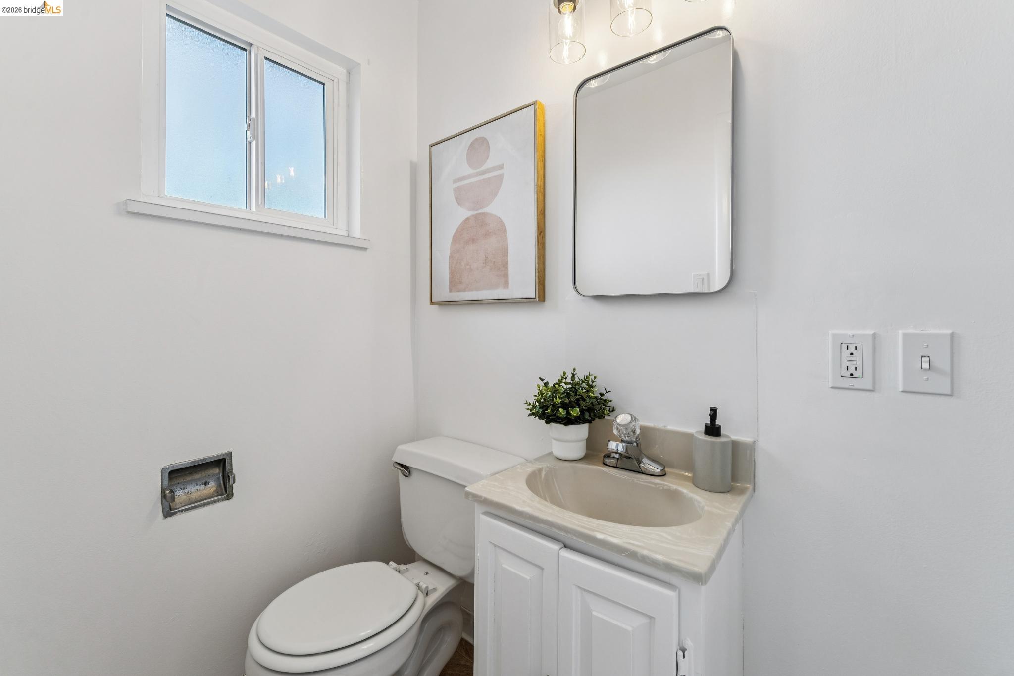 Bright bathroom with a white vanity and toilet, large mirror, and small window.