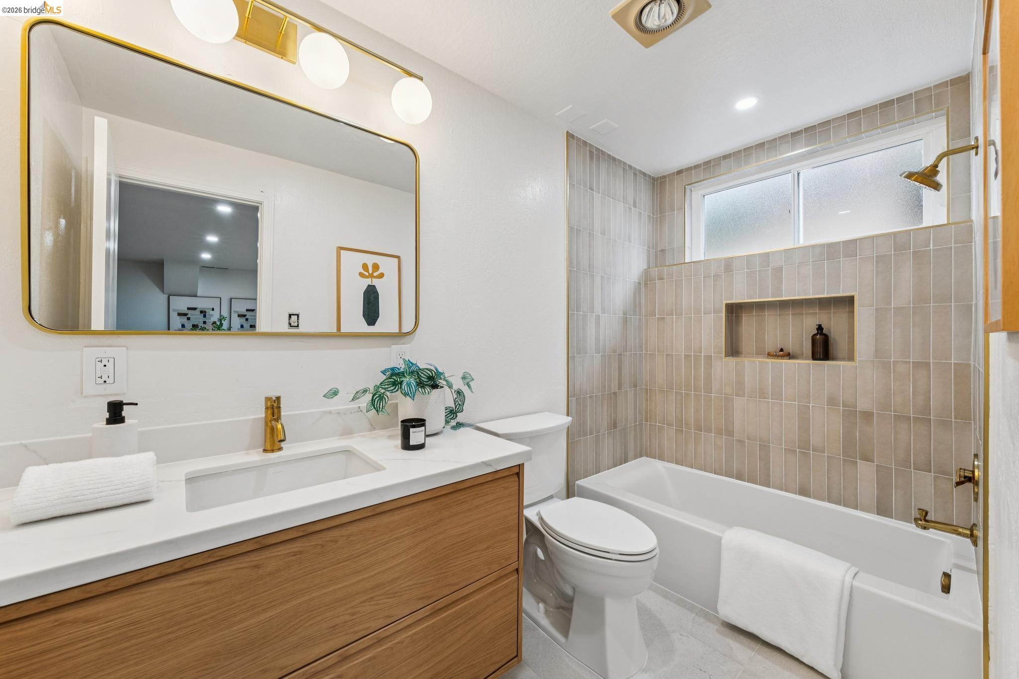 Updated bathroom with beige tiled tub surround, built-in niche, and wood-front vanity.