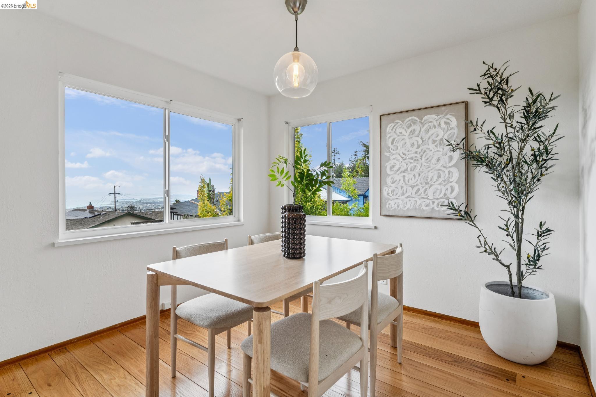 Staged dining room with corner windows, hardwood floors, and a distant urban view.