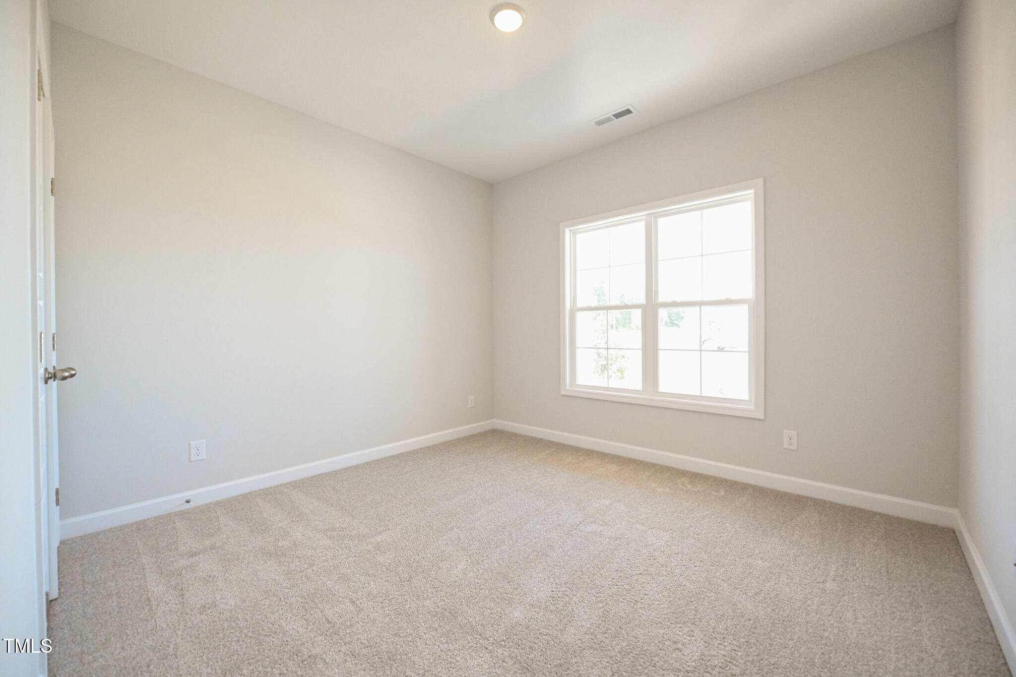 Empty bedroom with beige carpet and a large multi-pane window.