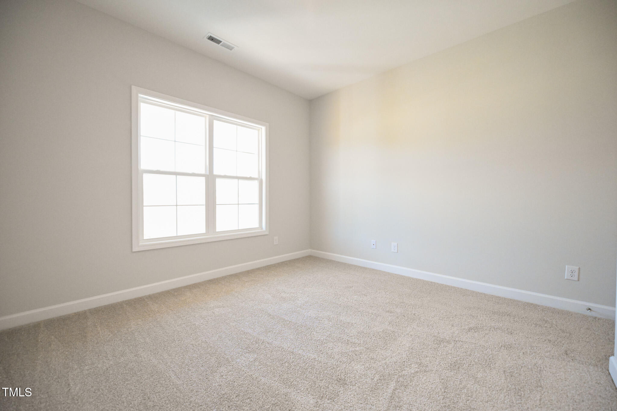 Vacant bedroom with beige carpet and a large double window.