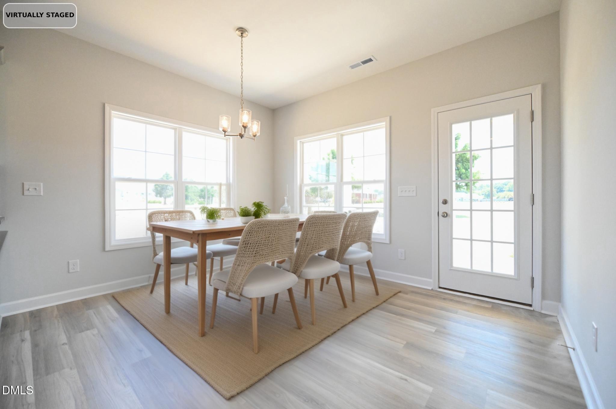 Dining room with a wooden table, woven chairs, chandelier, and large windows.