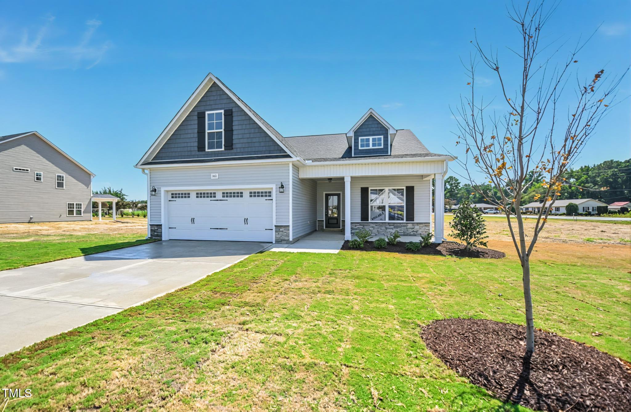 Gray-and-white house with a double garage, covered porch, and young tree in the front lawn.