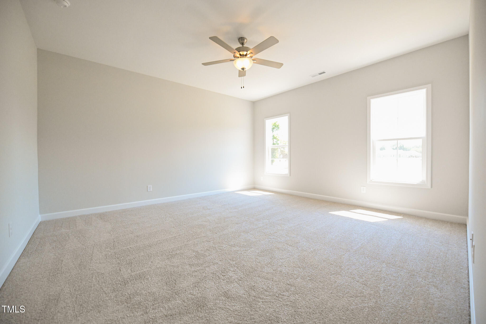 Vacant carpeted bedroom with two windows and a ceiling fan.