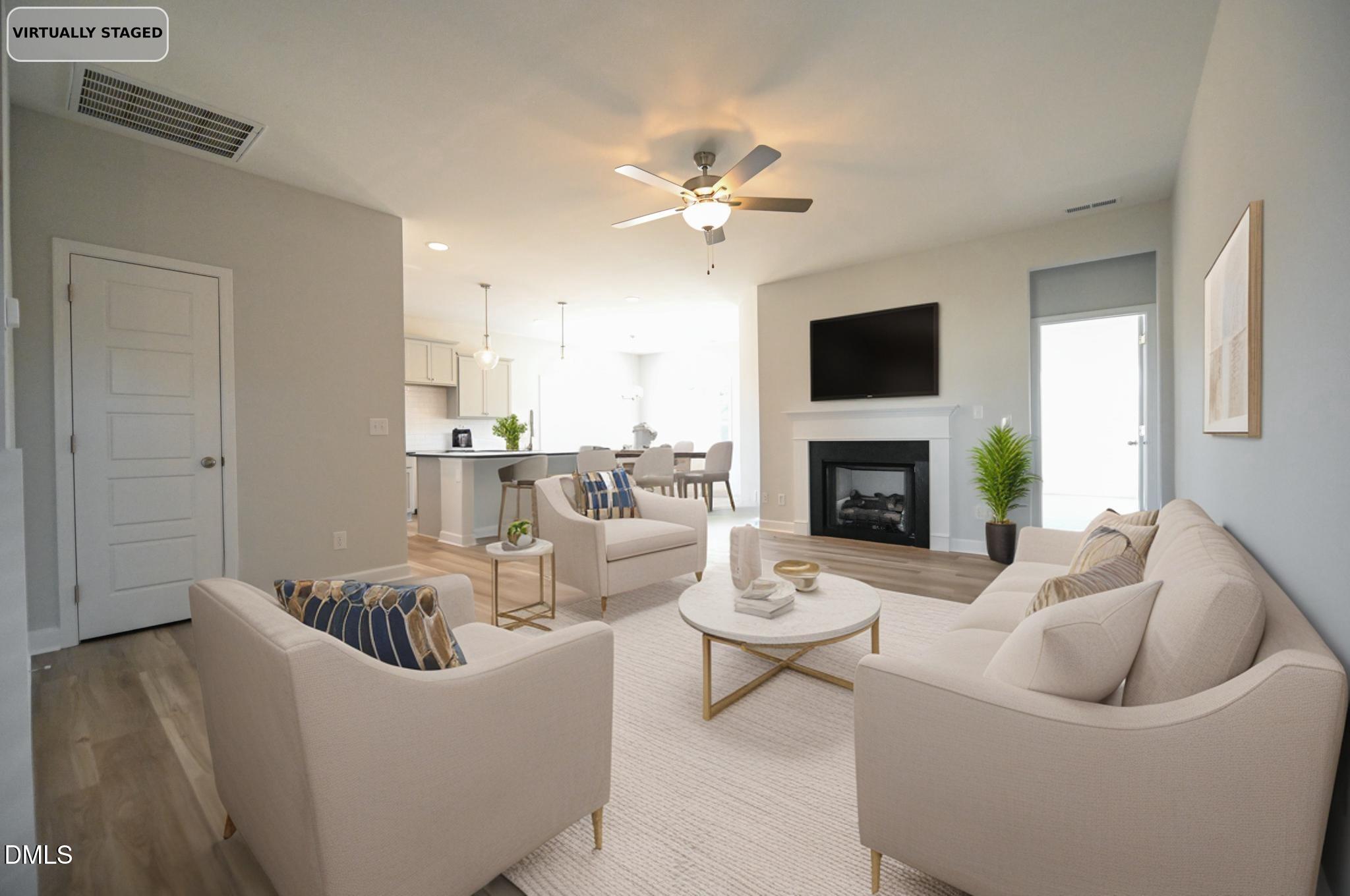 Virtually staged living room with cream seating, a fireplace, and an open kitchen and dining area.