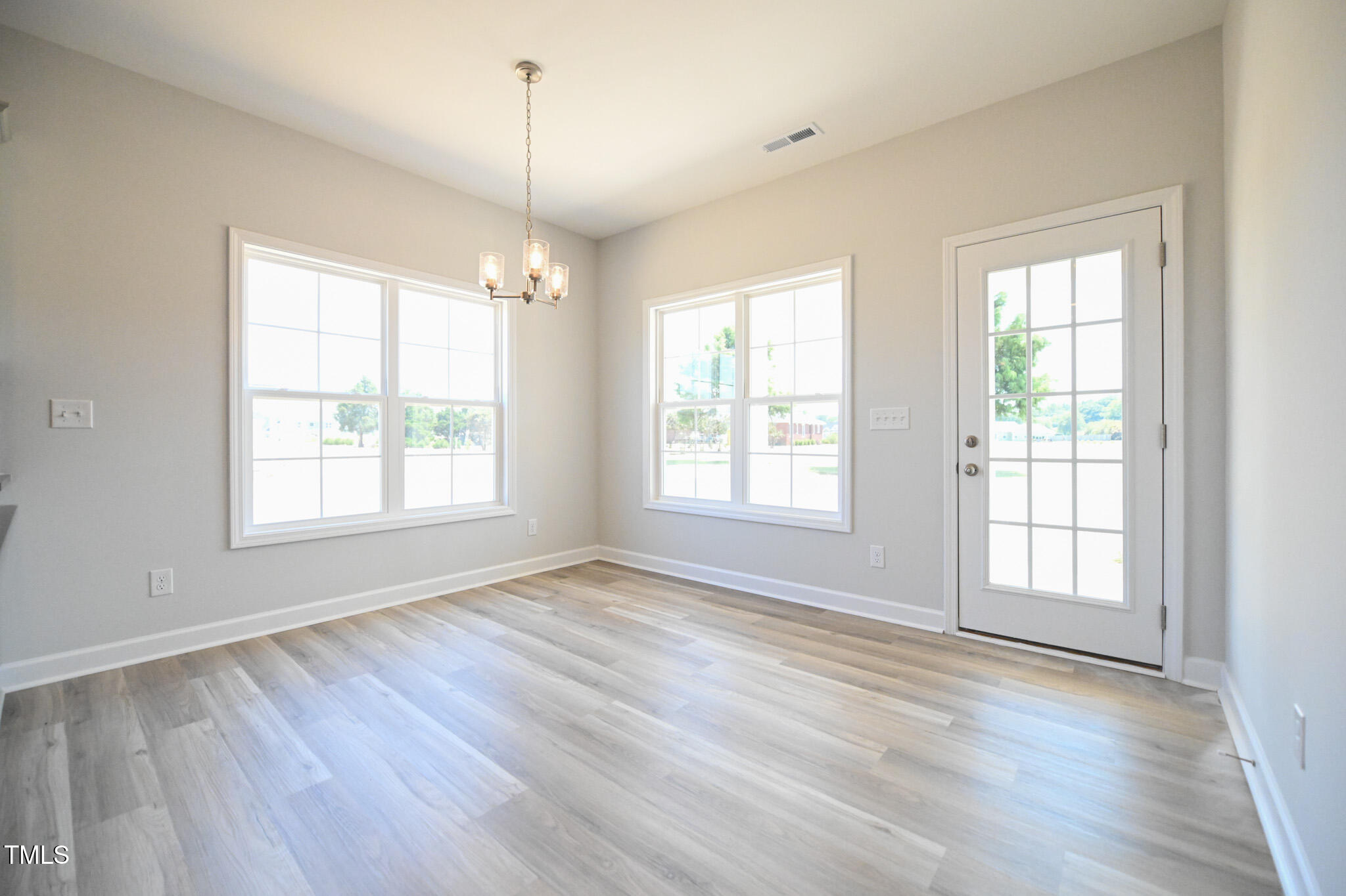 Empty dining area with gray wood-look floors, a chandelier, two windows, and a glass-paneled exterior door.