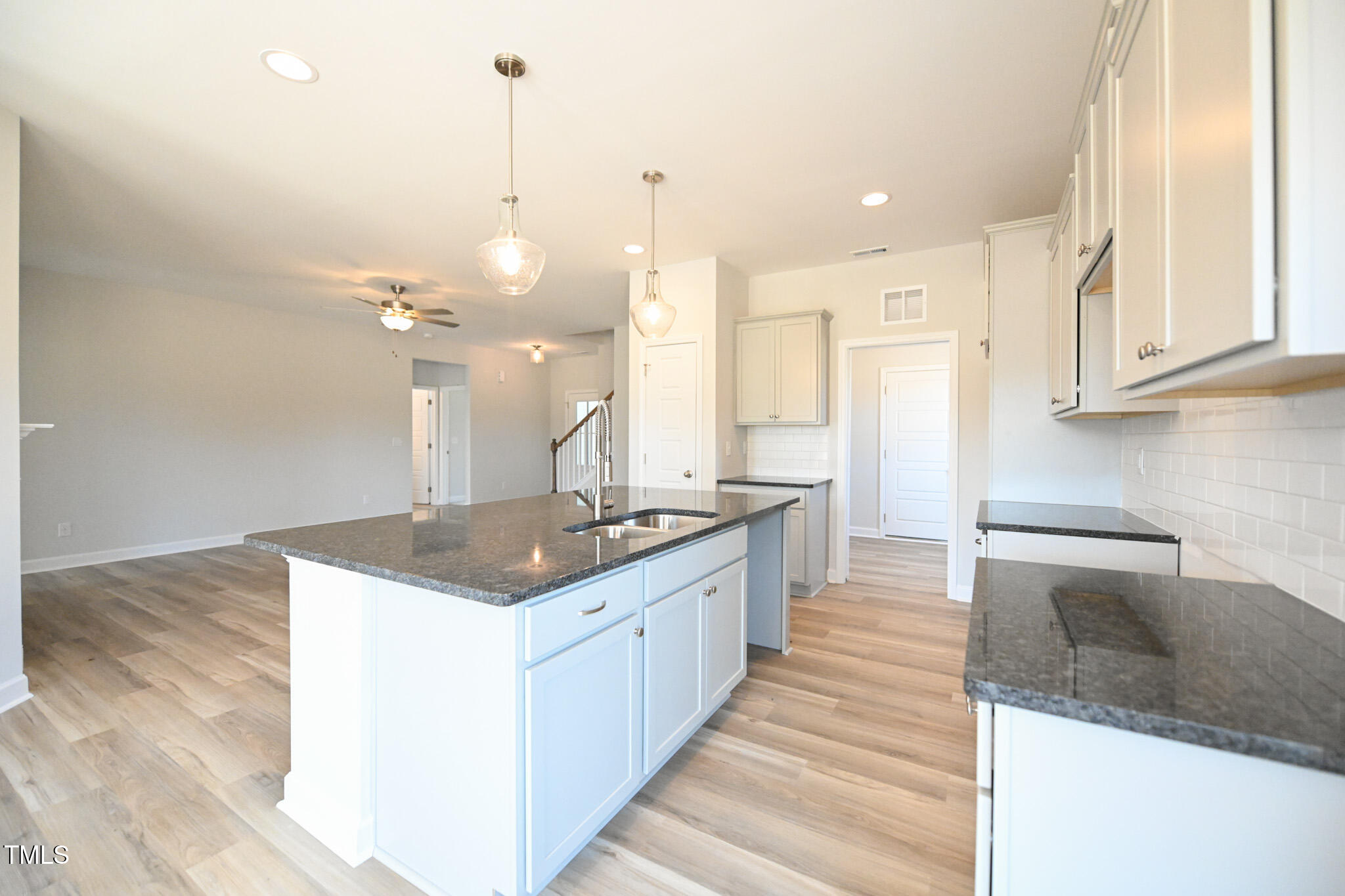 Unfurnished kitchen with a large dark-countertop island, white cabinets, and light wood-look floors.