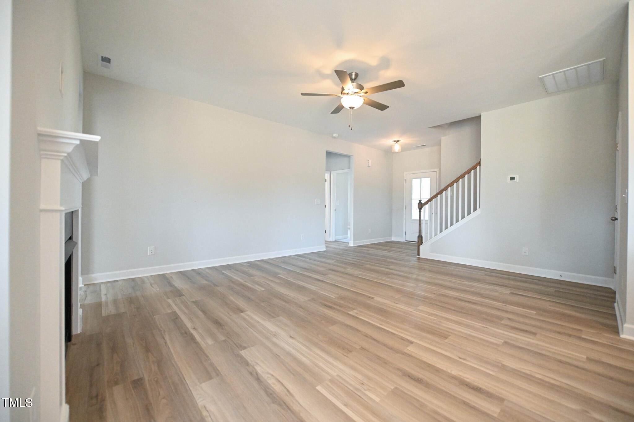 Empty living room with wood-look flooring, ceiling fan, and staircase.