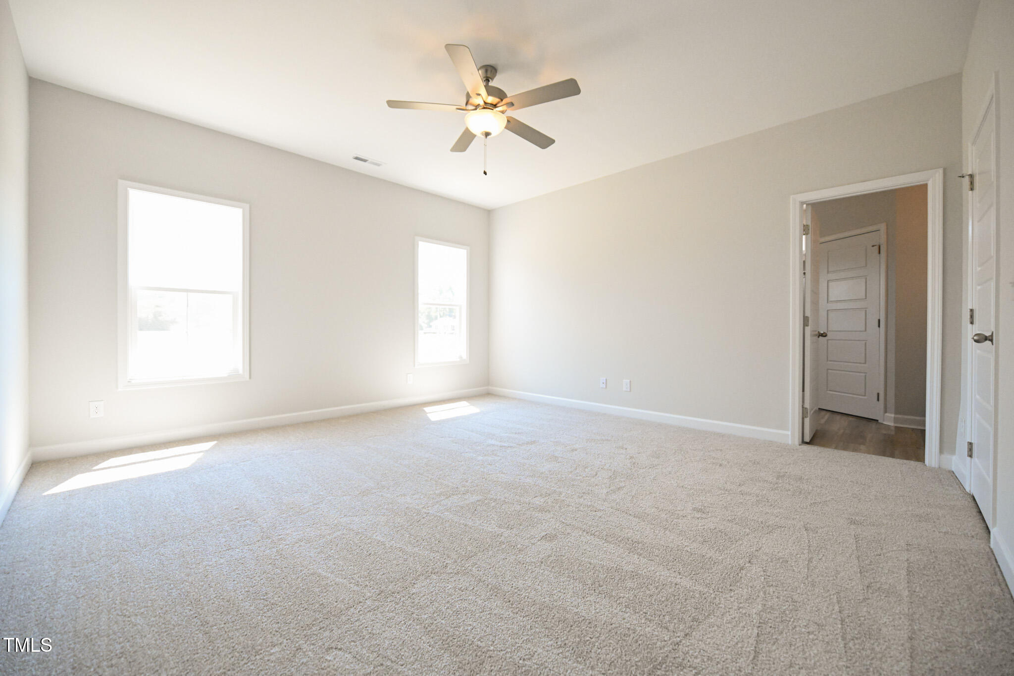 Empty carpeted bedroom with two windows and a lit ceiling fan.