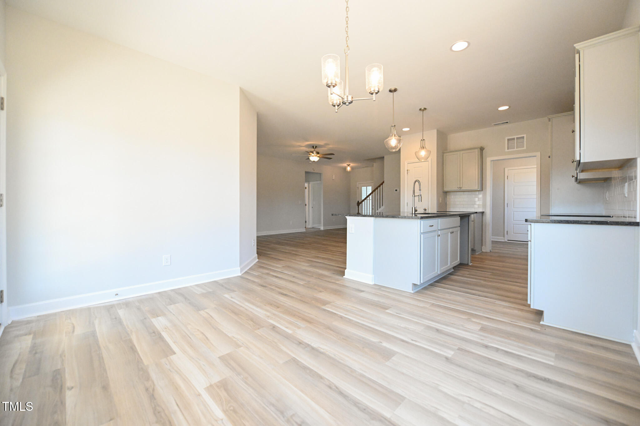 Open-plan kitchen with white cabinets, a dark-countertop island, light flooring, and a staircase.