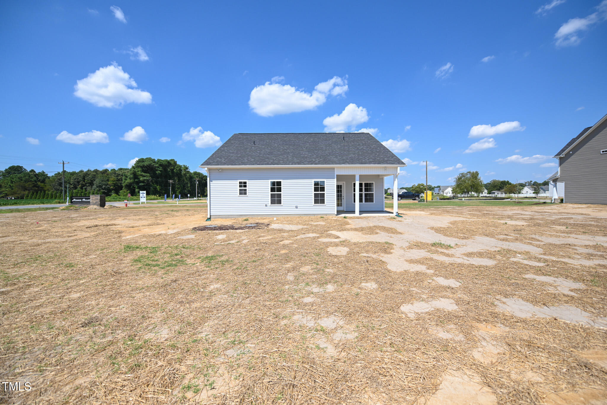 Light-sided house with a covered porch and mostly bare, unfinished yard.