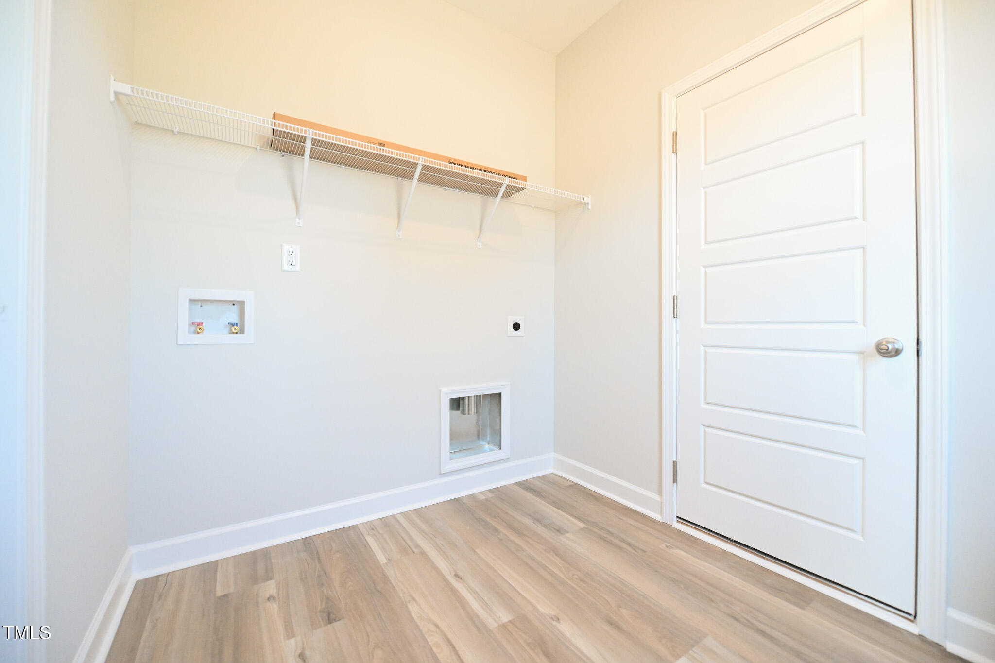 Empty laundry room with washer and dryer hookups, wire shelf, and white paneled door.