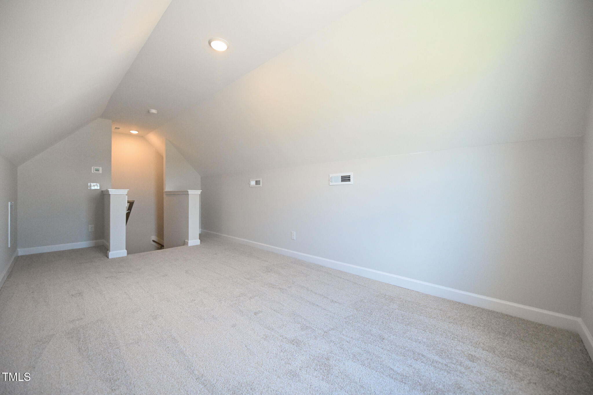 Unfurnished carpeted loft with a sloped ceiling and open stairwell.