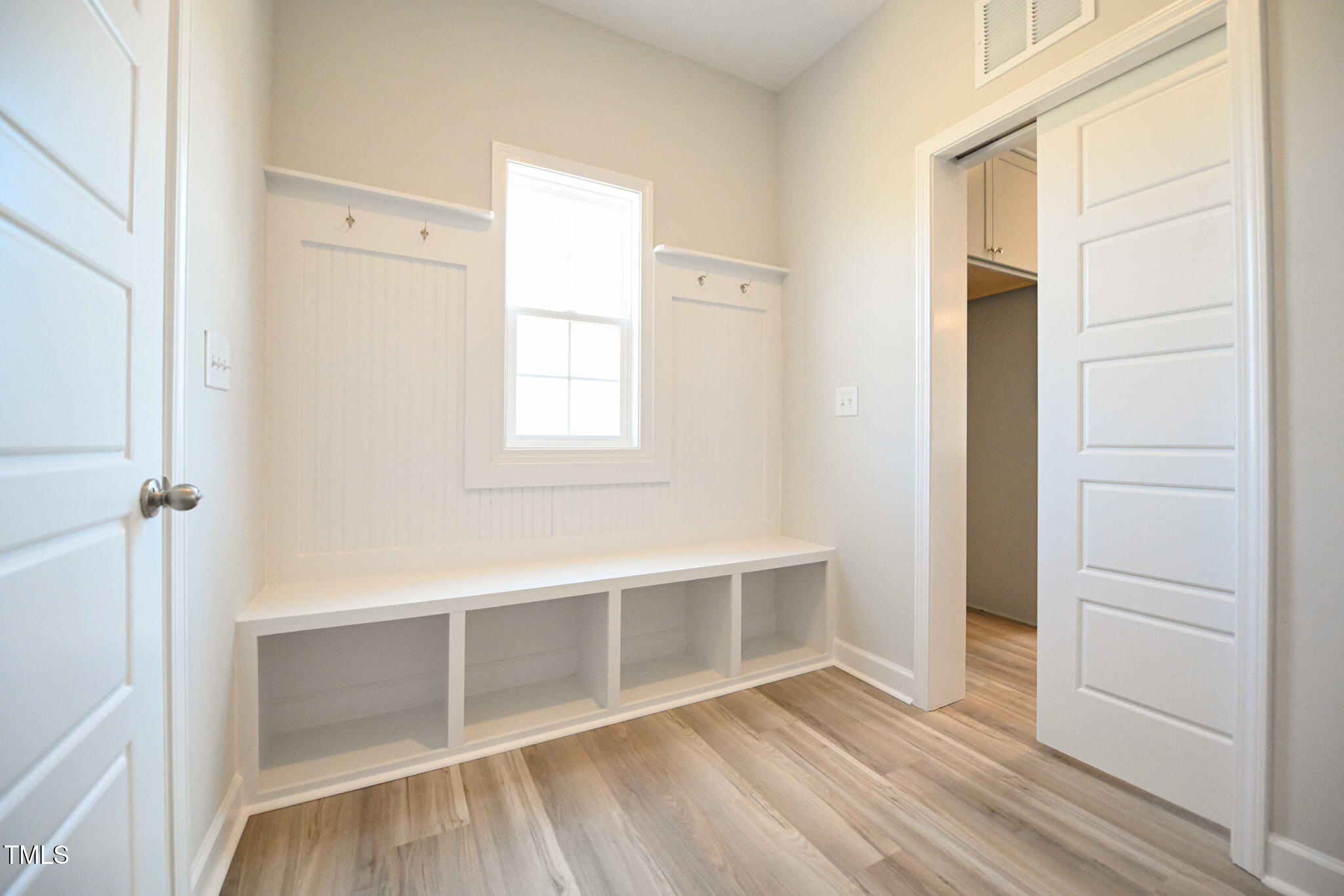 Bright mudroom with a built-in bench, open cubbies, beadboard hook panels, and a central window.