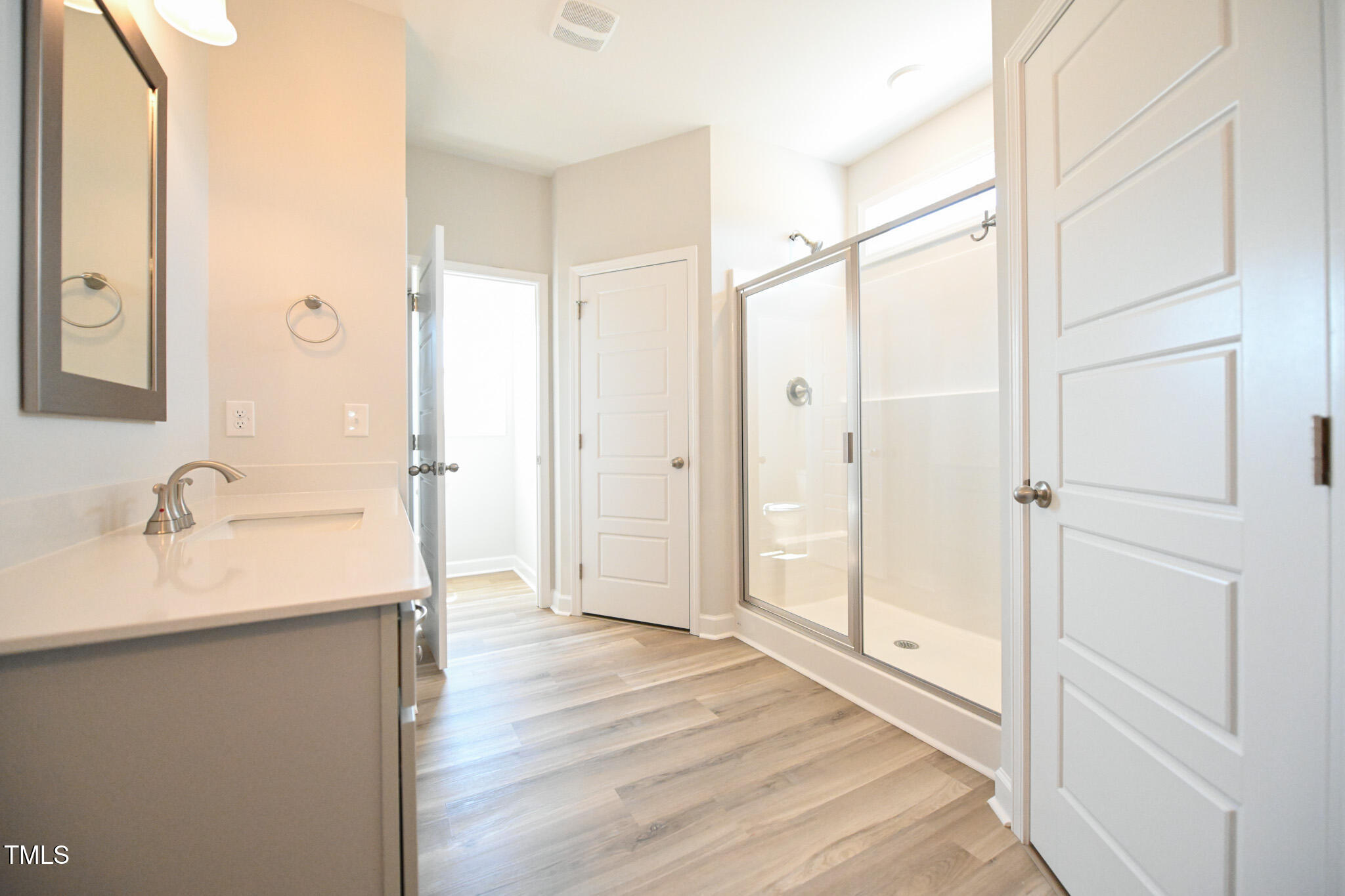 Bathroom with a glass-enclosed shower, white vanity, and gray wood-look flooring.