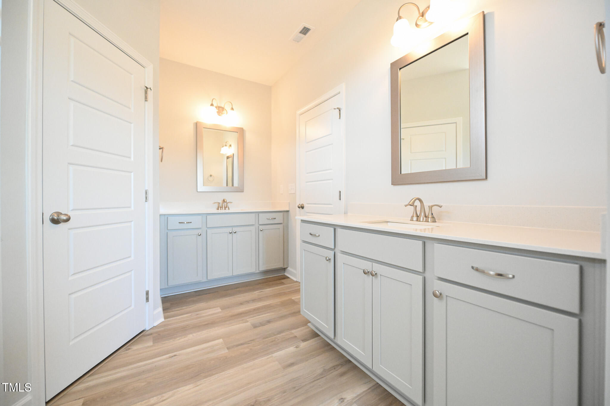 Bathroom with two light-gray vanities, white countertops, framed mirrors, and wood-look flooring.