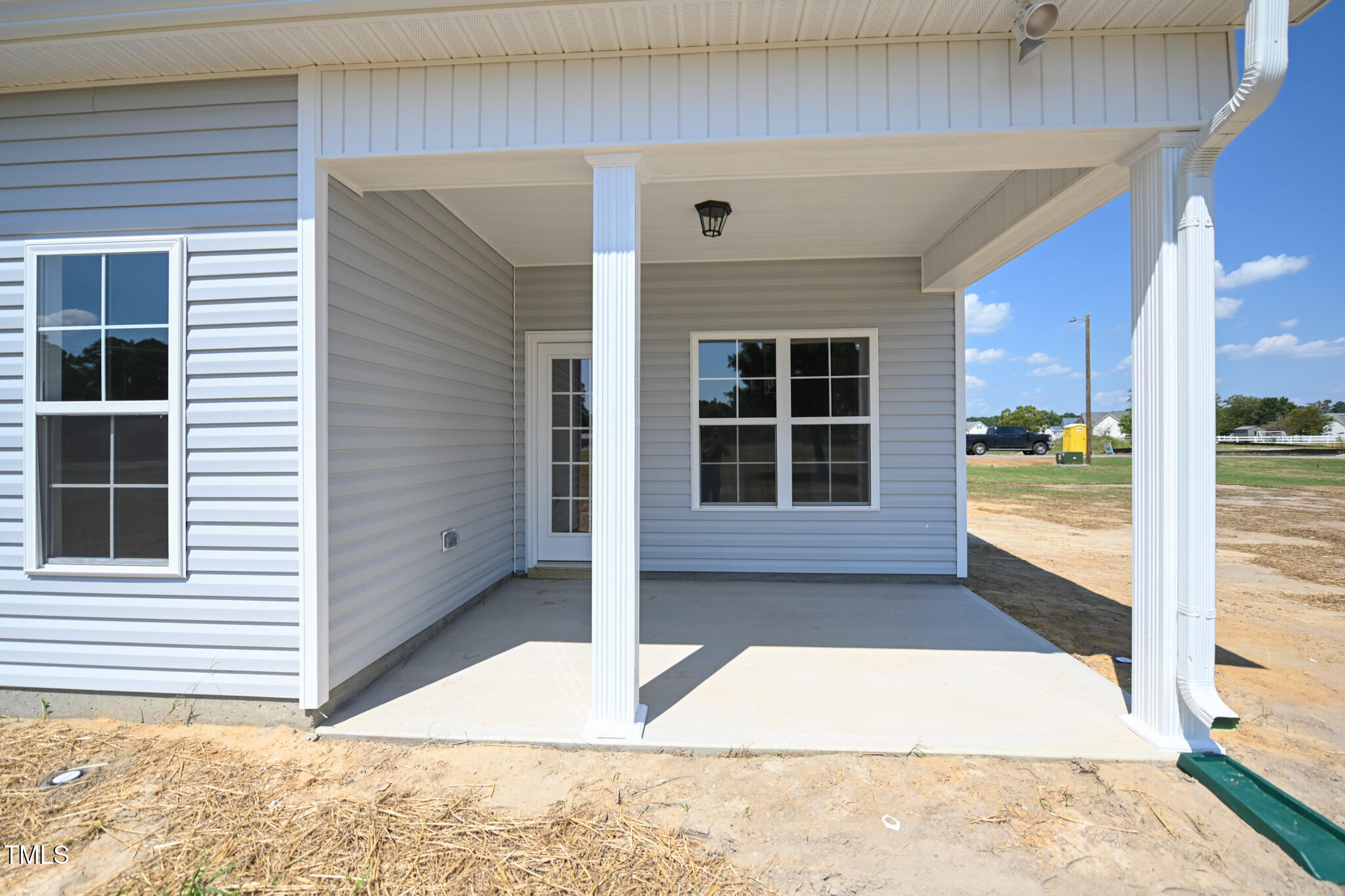 Covered concrete porch with white columns, gray siding, and a glass-paneled door.