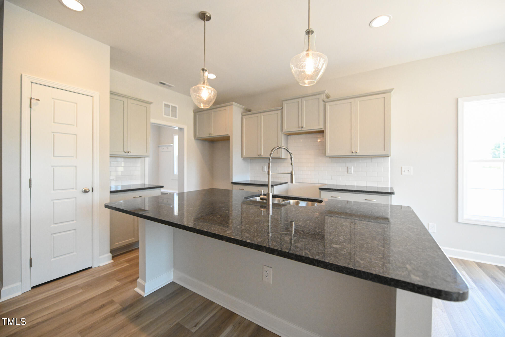 Vacant kitchen with a large dark granite island, spring-coil faucet, gray cabinets, and glass pendant lights.