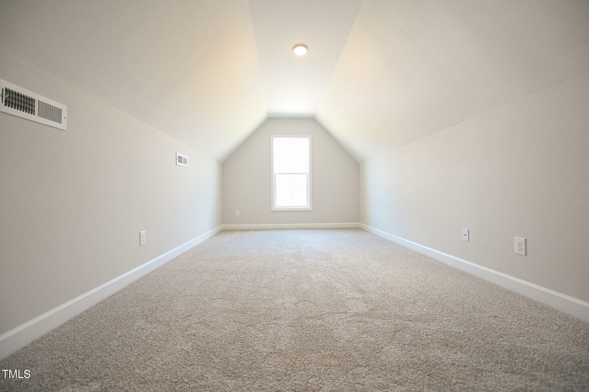 Empty carpeted room with a high sloped ceiling and a window at the far end.