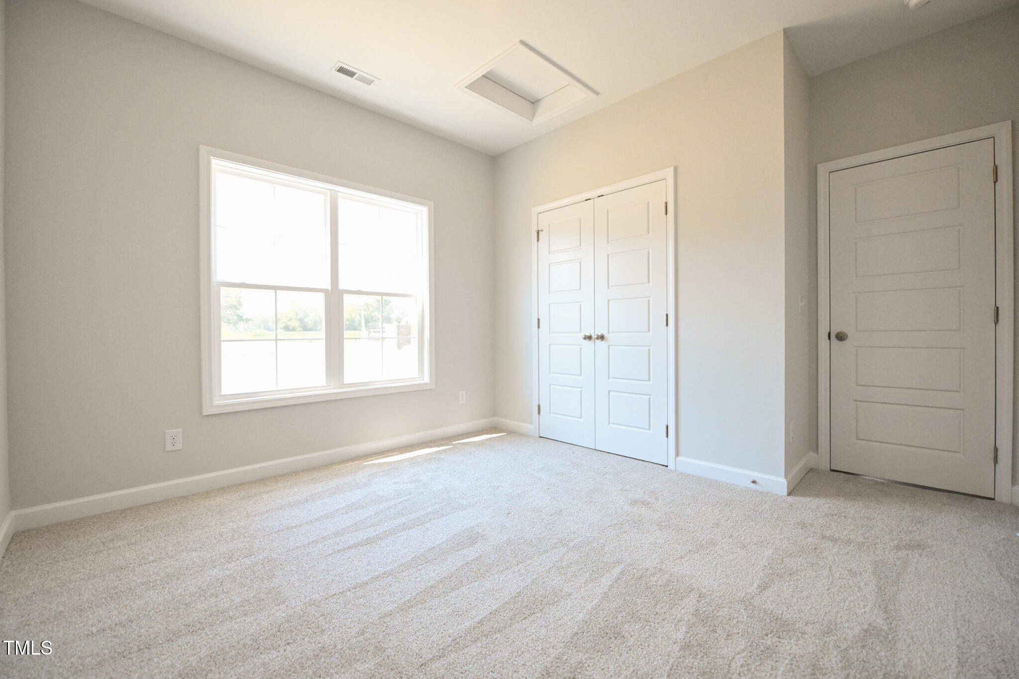 Empty bedroom with beige carpet, a large window, and double closet doors.