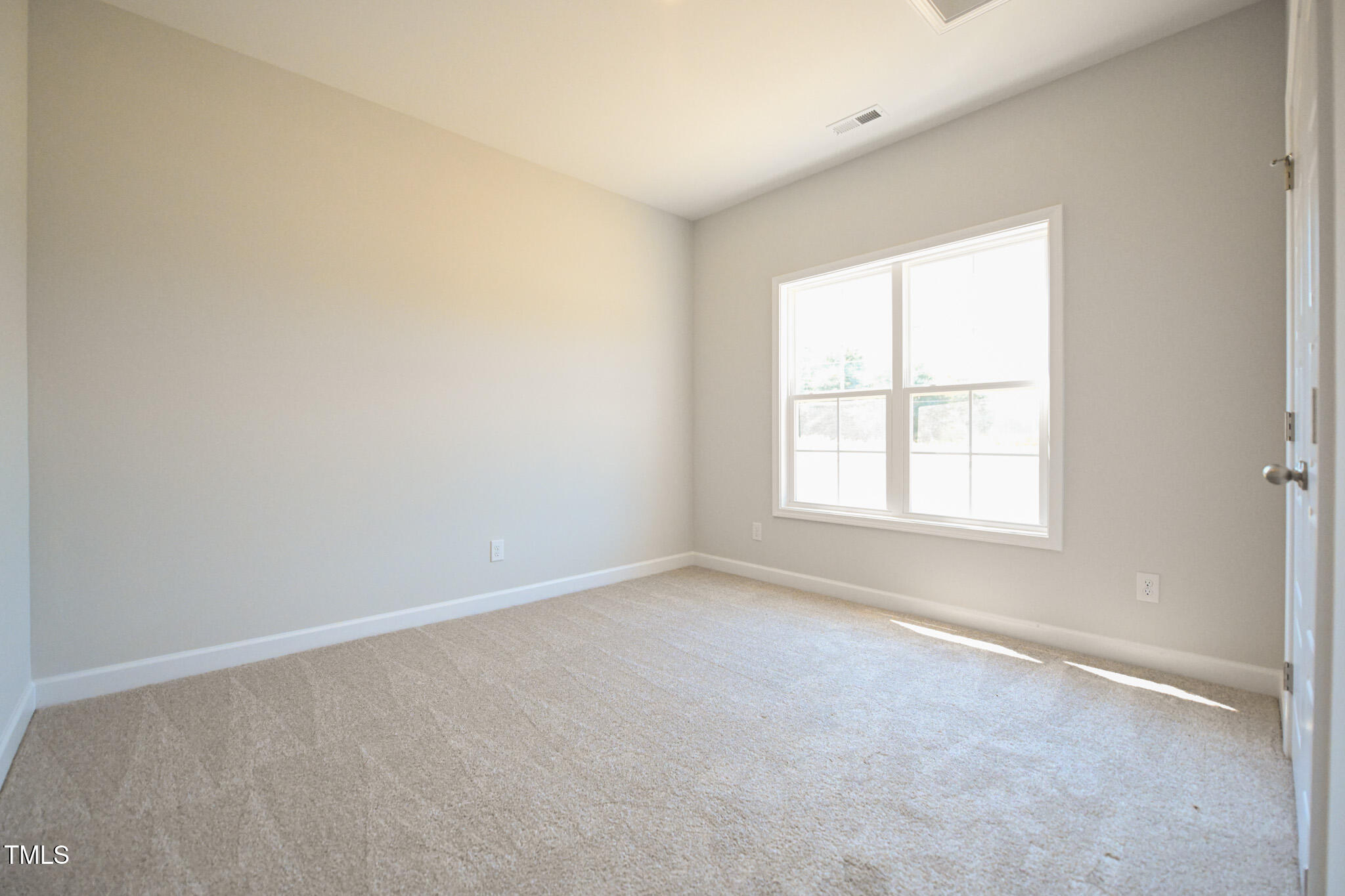 Empty carpeted bedroom with neutral walls and a large double window.