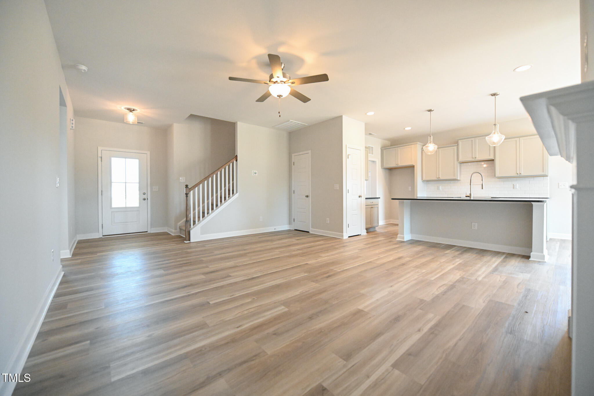 Vacant open-plan living room and kitchen with wood floors, staircase, and large island.