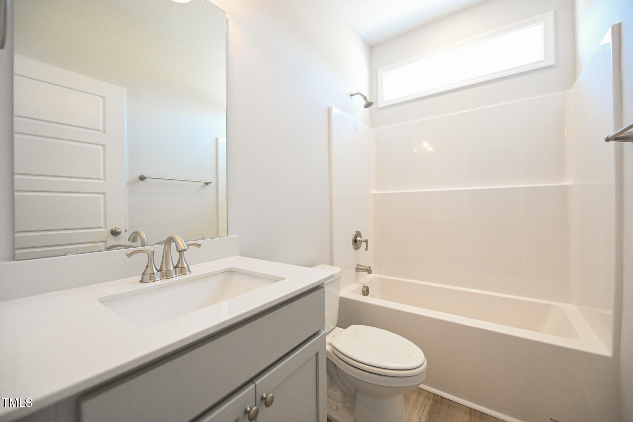 Bathroom with a gray vanity, large mirror, white tub and shower, and high horizontal window.