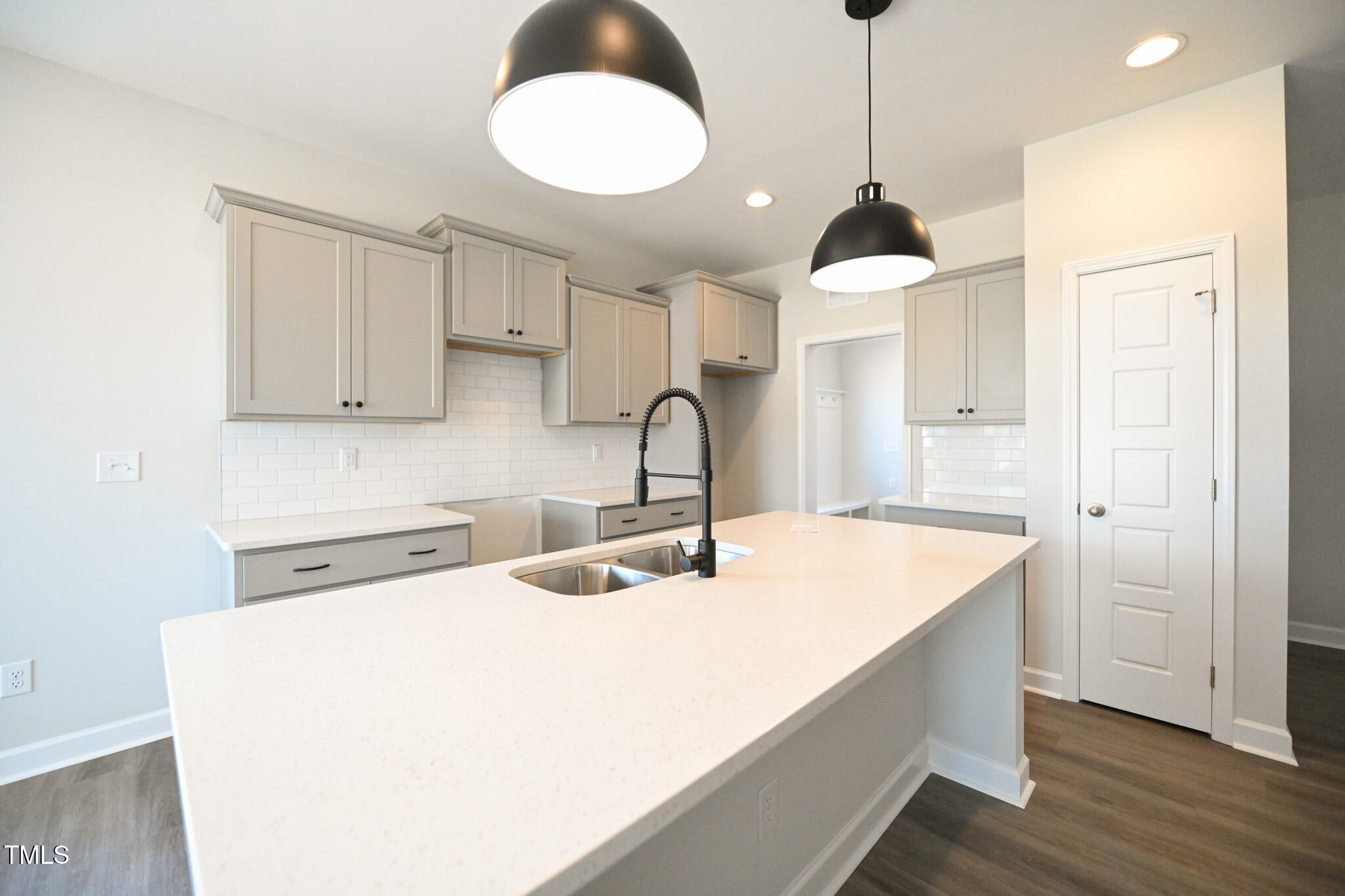 Kitchen with a large white quartz island, gray cabinets, subway tile backsplash, and black pendant lights.