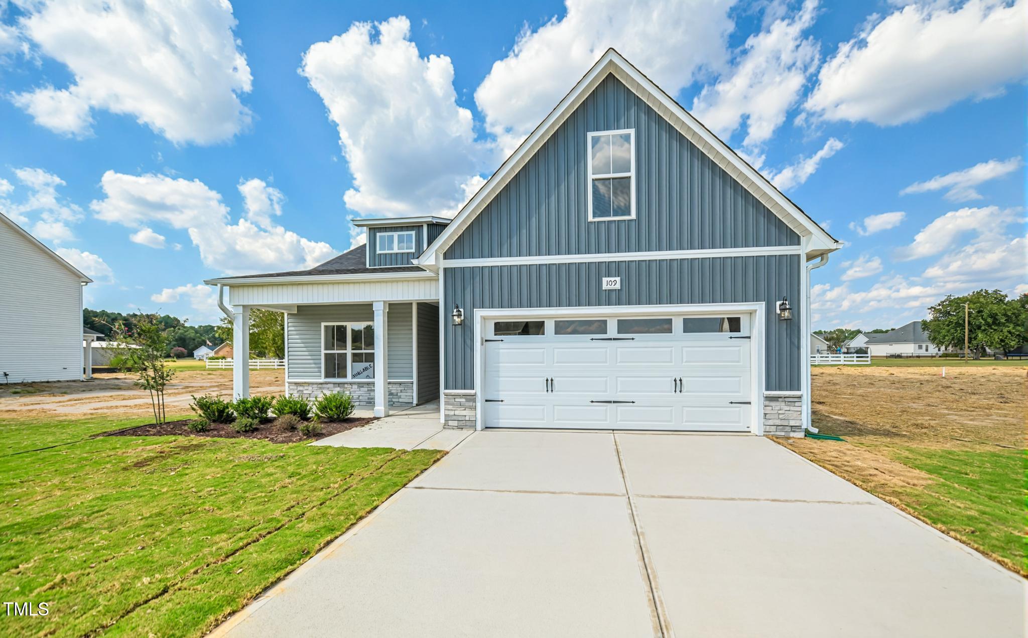 Blue-gray gabled house with white trim, a two-car garage, covered porch, and broad concrete driveway.