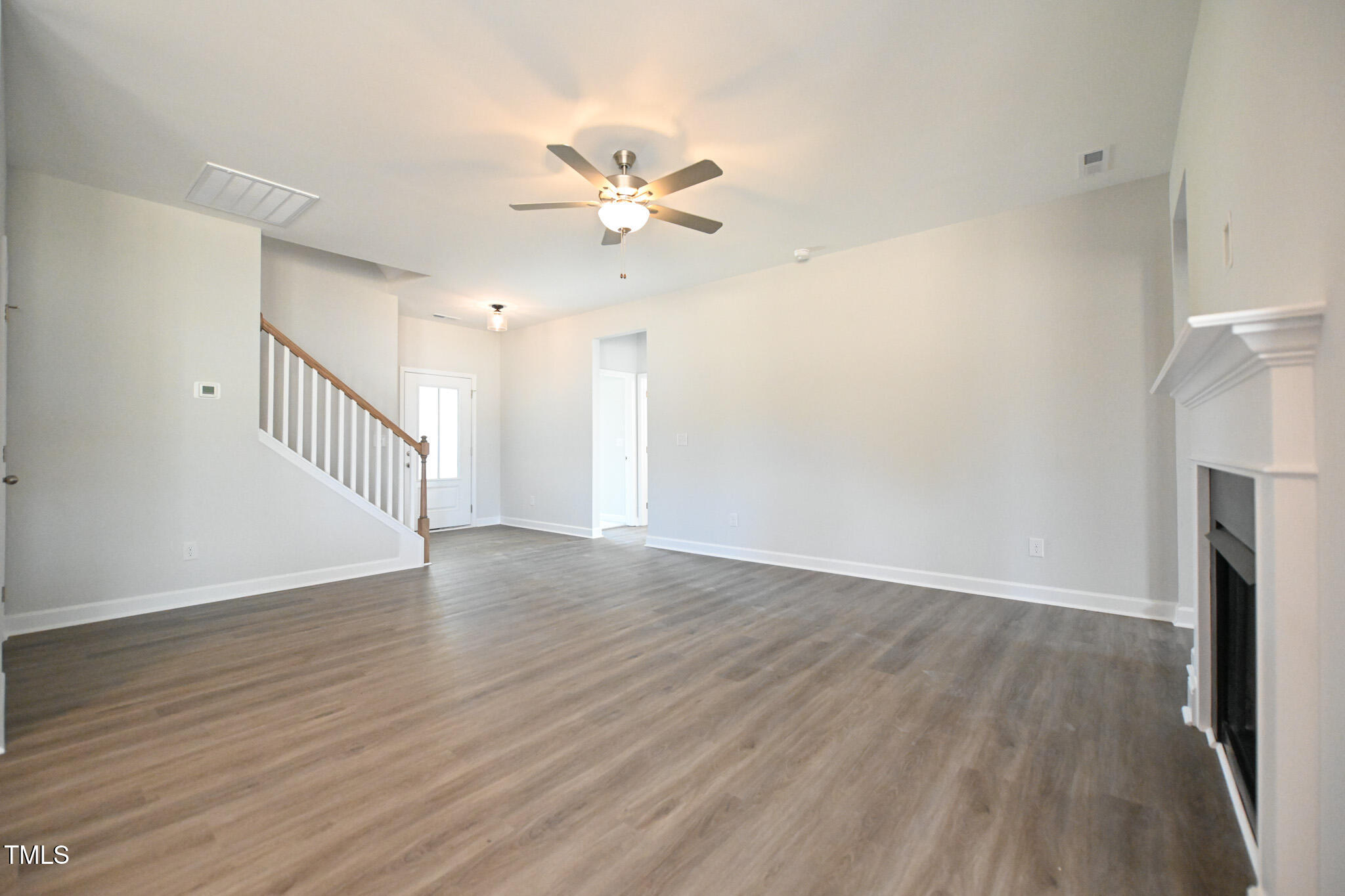 Empty living room with gray wood-look floors, a white fireplace, and a staircase with a wood handrail.