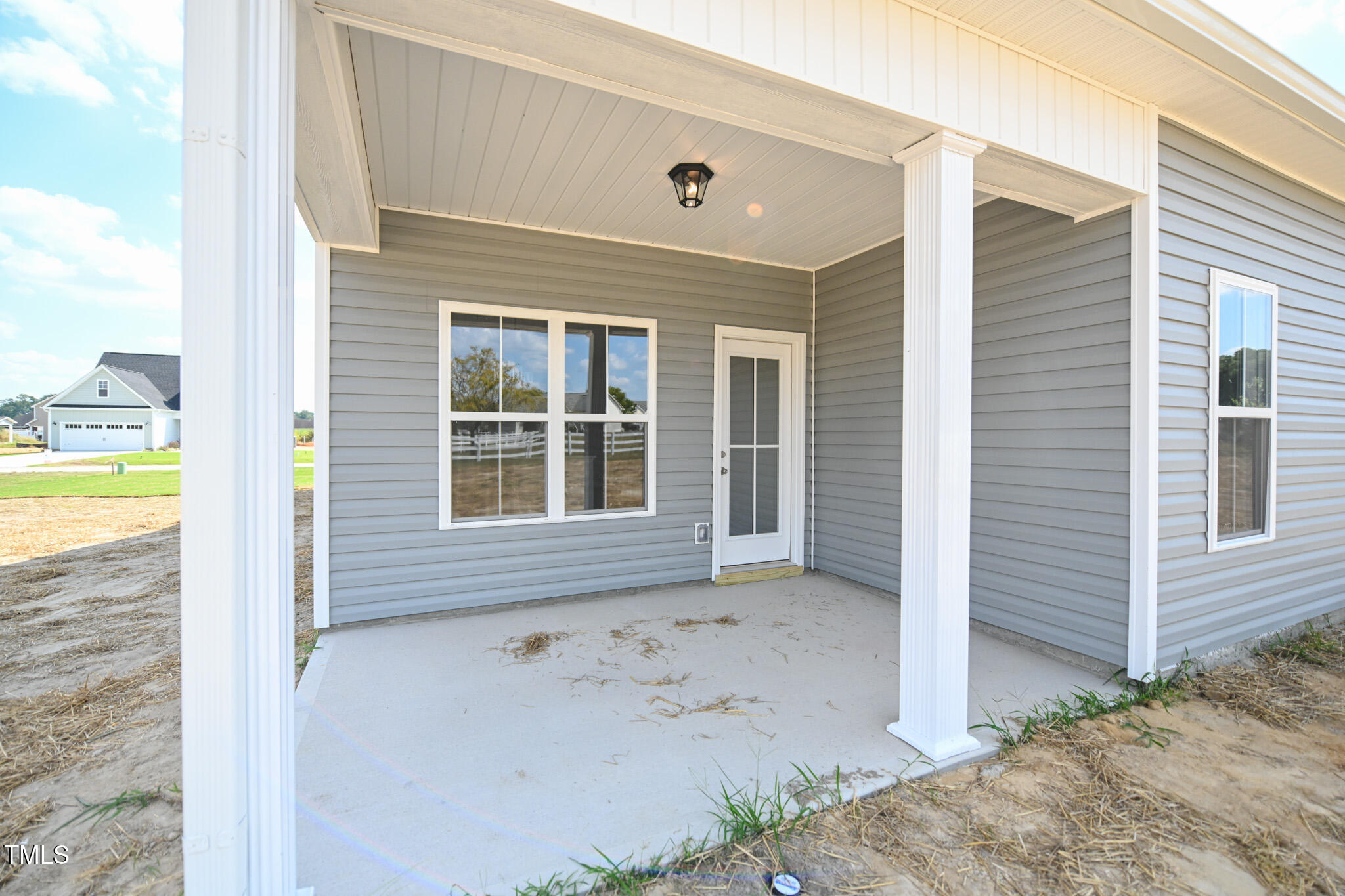 Gray-sided home with a covered concrete porch, white columns, and a glass-paneled front door.