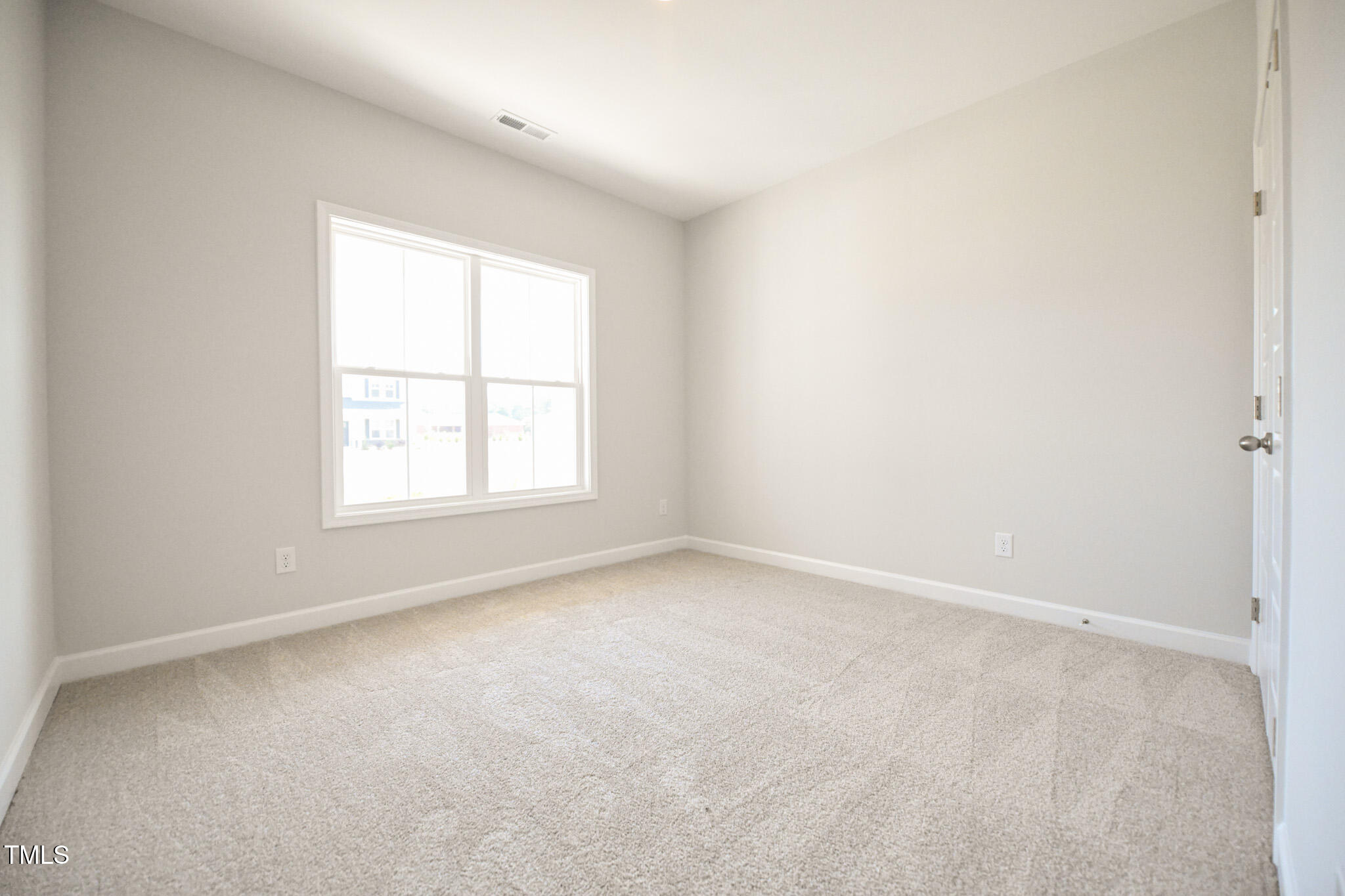 Empty carpeted bedroom with pale gray walls and a large double window.