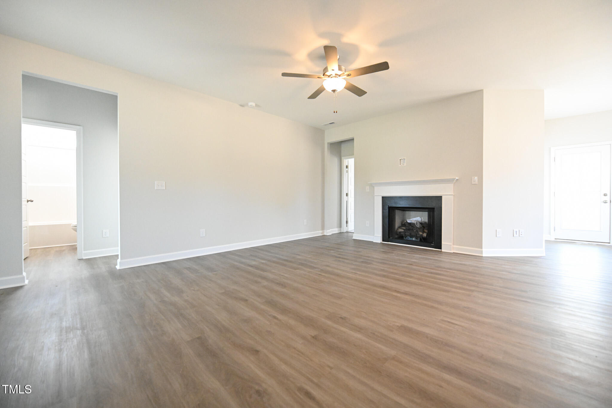 Empty living room with a white-trimmed fireplace, ceiling fan, and gray-brown plank flooring.