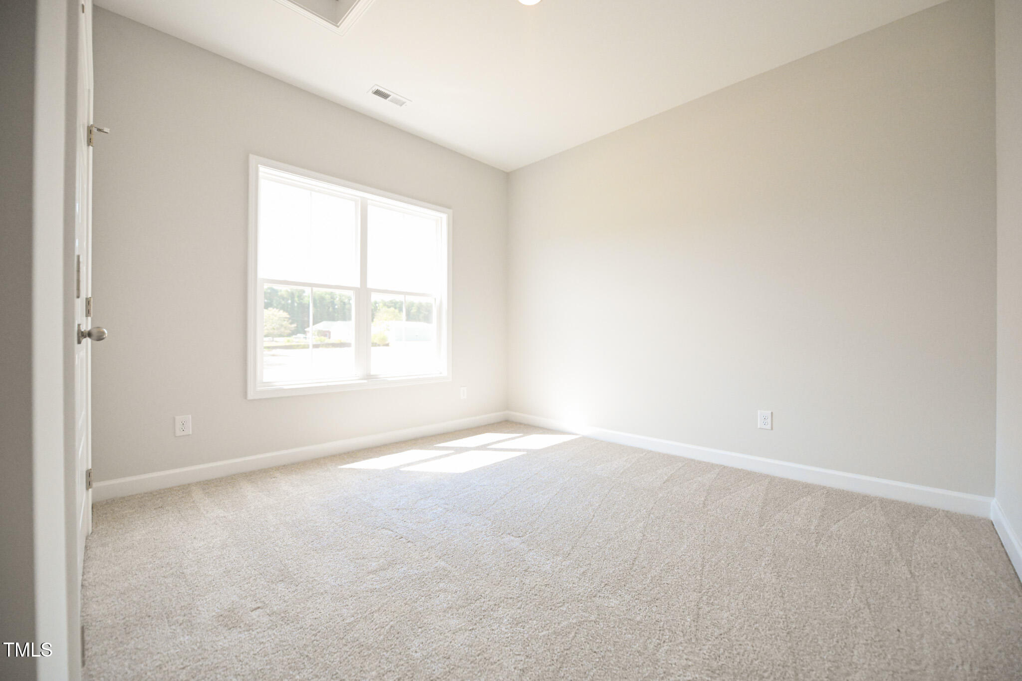 Empty carpeted bedroom with a large window and sunlight across the floor.